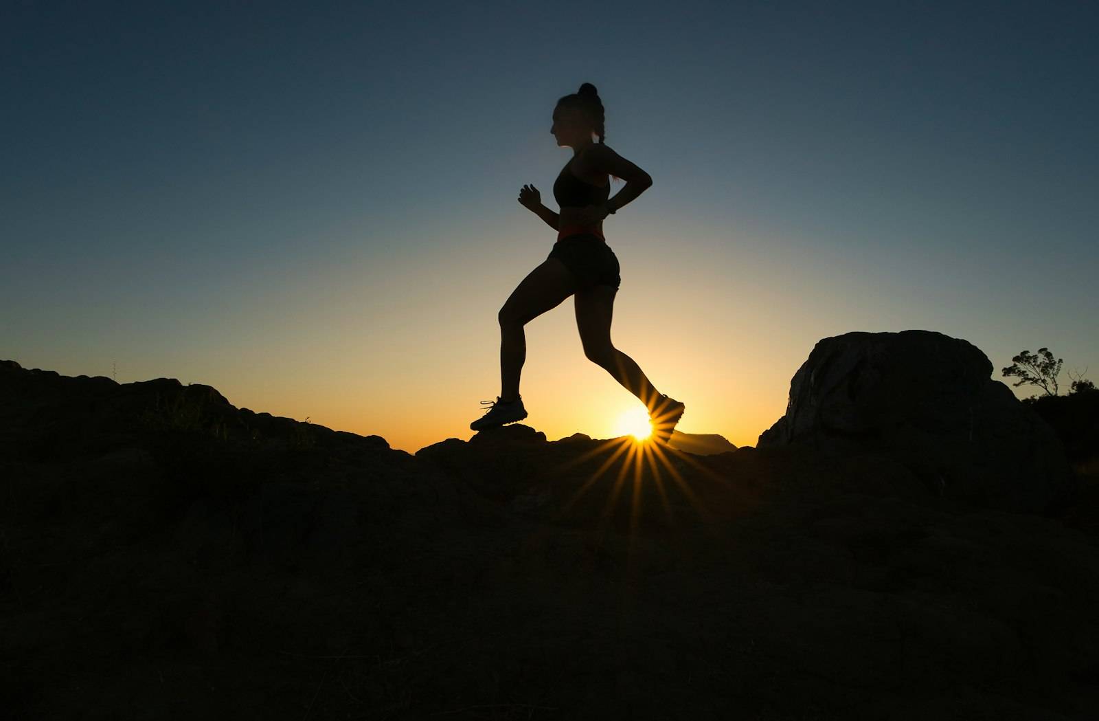 Silhouette of a runner on a rocky trail against a low sun